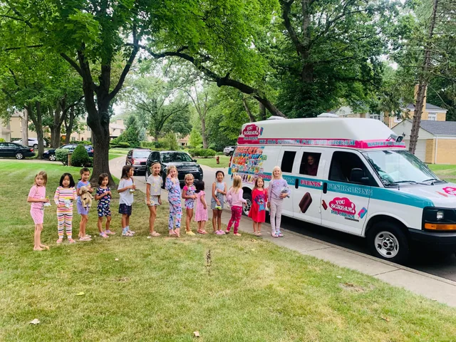 A class of young children lined up beside the truck on the grass at a daycare event